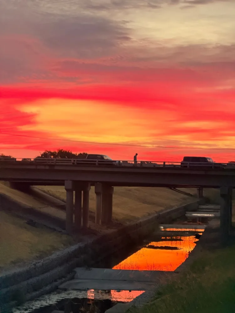 A red sunset over a highway bridge and a creek in Fort Worth